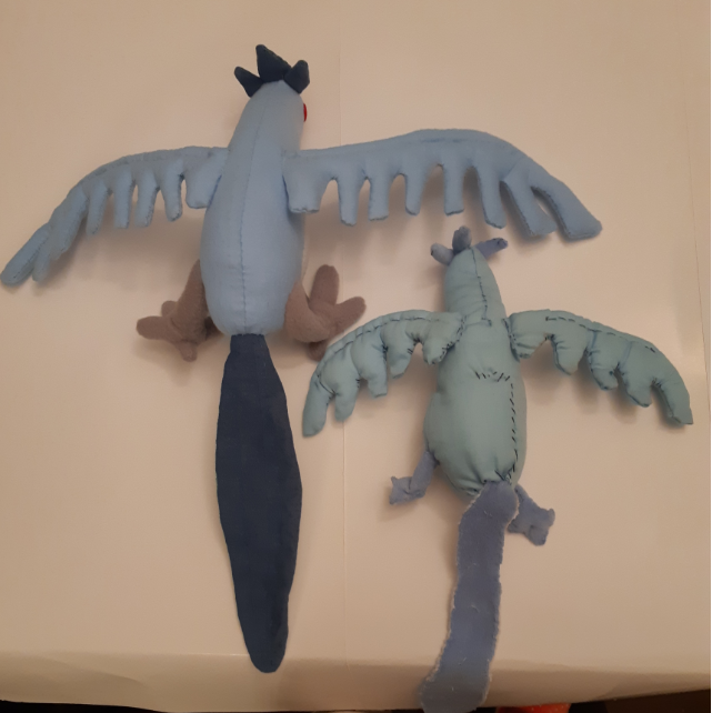 Side-by-side comparison of the two Articuno plush toys, the backs of both plushies are shown. The old one has a noticeable L-shaped stitched scar on its back.
