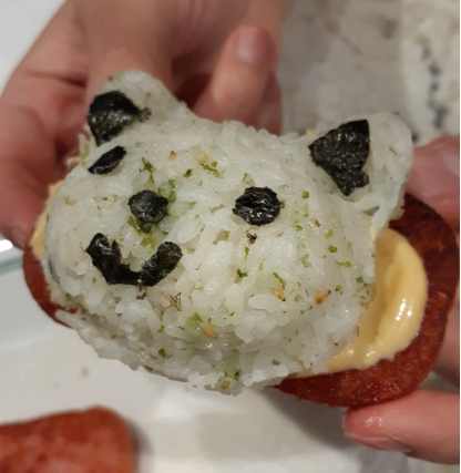 Cat shaped rice balls, topped with spicy mayonnaise and seaweed shapes, and sitting on a slice of spam