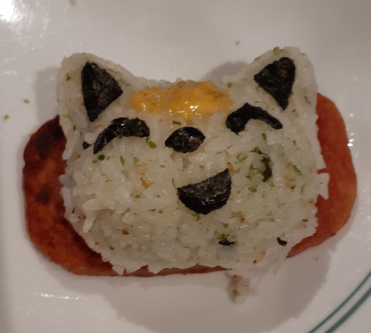 Cat shaped rice balls, topped with spicy mayonnaise and seaweed shapes, and sitting on a slice of spam