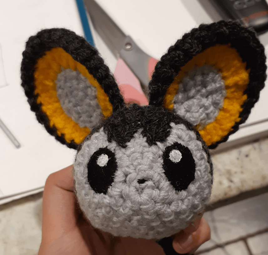 Amigurumi Emolga, front view of face with eyes painted and peak attached