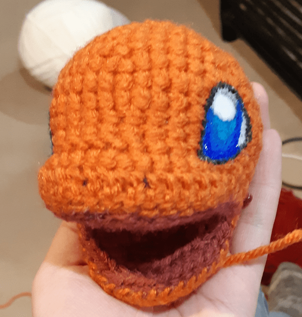 Amigurumi Charmander, front view of assembled head with partially painted eyes.