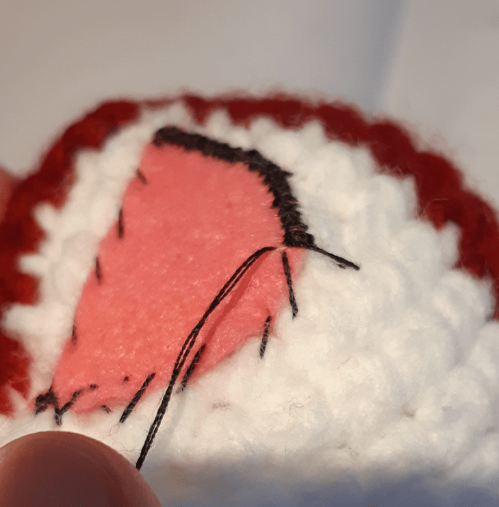 Amigurumi felt detailing : eye piece going through second round of stitching, placing the stitch just outside the edge to the nearest crocheted peak