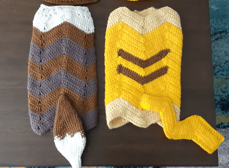 Completed blanket sets of the eevee and pikachu. Pikachu blanket features two brown stripes on a yellow and cream zig zag blanket and a zig zag tail. Eevee blanket features a brown and grey-brown striped zig zag blanket with off-white on one side and the tail on the opposite end.