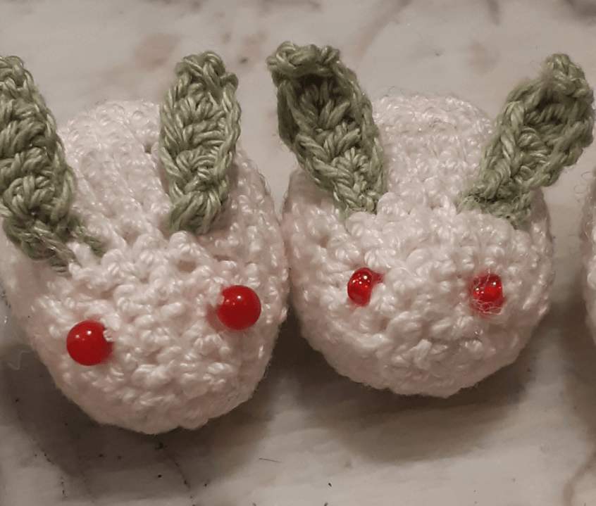 A comparison of two crocheted snow bunnies. One has stone bead eyes that are uniformly round, while the other one has glass beads with flattened ends.