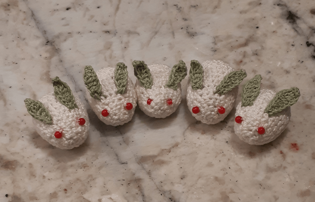 A completed set of five snow bunnies, made out of one white oval, two green leaf bits, and two red glass beads. They are facing forward, forming a semi-circle.