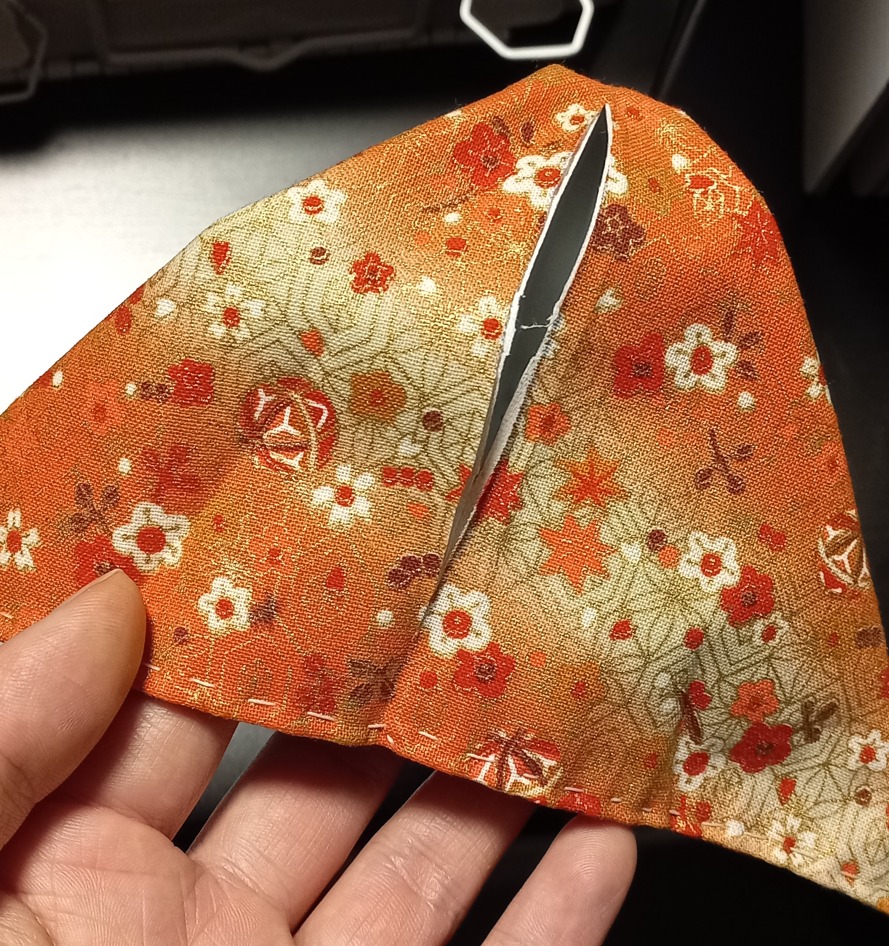 Image of the smaller orange fish pouch, showing the opening that was cut mid-fabric, for the installation of the zipper. The opening is concentrated in the area that resembles the backbone of the fish.
